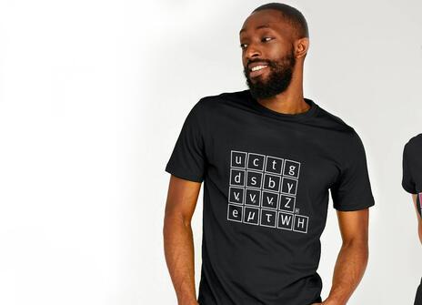 A man is wearing a black T-shirt with a white drawing of the standard model on it, a woman is next to him weaing a black t-shirt with a colourful graphic of a standard model on it