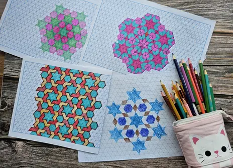 Some colourful geometric drawings on paper and a pencilcase filled with colouring pencils