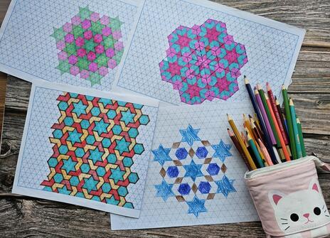 Some colourful geometric drawings on paper and a pencilcase filled with colouring pencils