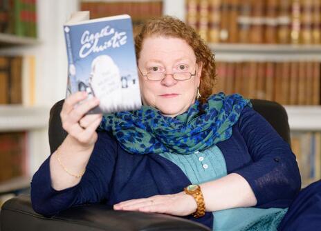 Sue Black in the Ri library holding up an Agatha Christie book