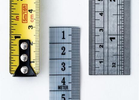 A close up of the end of a yellow tape measure, grey flexible measure and metal ruler.