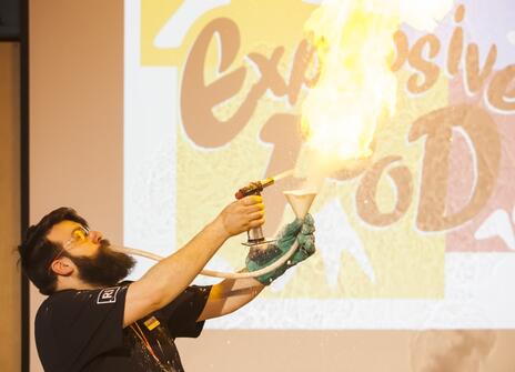 A man blows flour into a blowtorch, creating a giant fireball