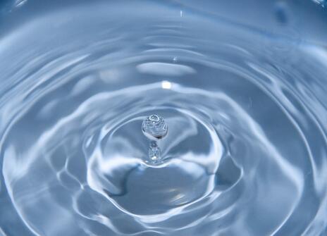 a droplet of water bounces out of some water, creating ripples. 