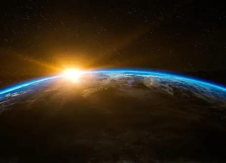 A picture of half the Earth from space. It is in shadow. The sun is just peaking above the horizon.