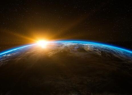 A picture of half the Earth from space. It is in shadow. The sun is just peaking above the horizon.