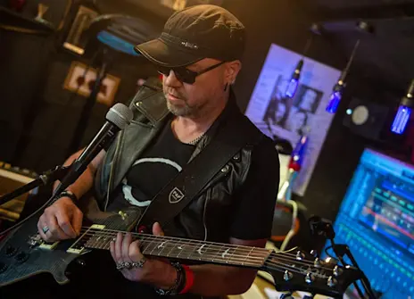 Physicist and musican Bob Coecke wearing a baseball cap holding a guitar in front of a microphone