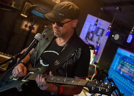 Physicist and musican Bob Coecke wearing a baseball cap holding a guitar in front of a microphone
