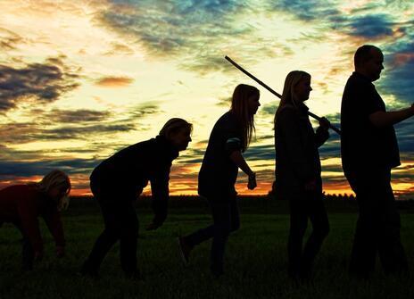 black profiles of human like structures against a sunset