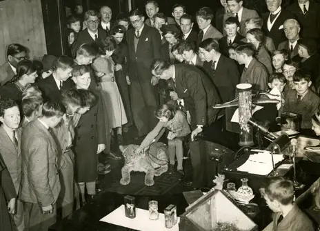 A black and white photo showing Julian Huxley surrounded by a crowd of people. It is part of his Christmas Lecture series from 1937.