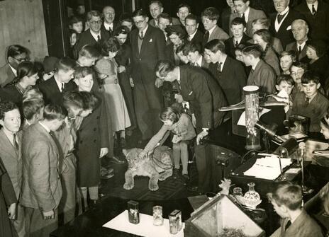 A black and white photo showing Julian Huxley surrounded by a crowd of people. It is part of his Christmas Lecture series from 1937.