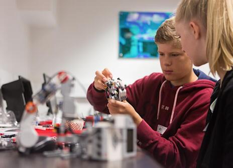 Two students, with one on the left handling part of a robot