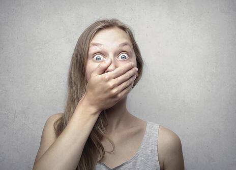 A woman with eyes wide in shock, covering her mouth with her hand
