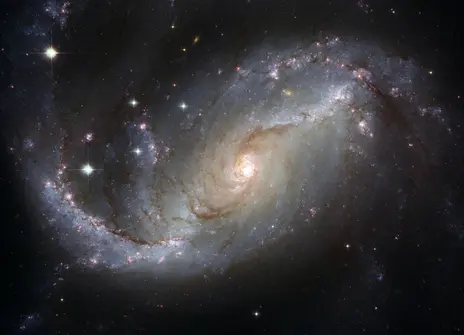A  view of a spiral galaxy, NGC 1672, unveils details in the galaxy’s star-forming clouds and dark bands of interstellar dust. 