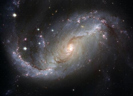 A view of a spiral galaxy, NGC 1672, unveils details in the galaxy’s star-forming clouds and dark bands of interstellar dust.
