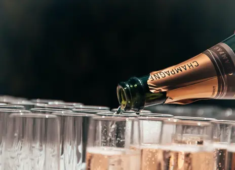 An open bottle of champagne is pouring champagne into lots of flute glasses.
