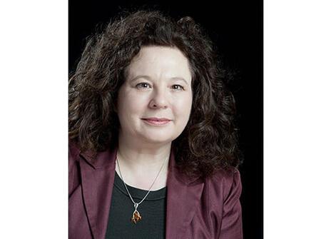 Kate Hamilton, she has shoulder length curly brown hair and is wearing a black top and a mauve jacket