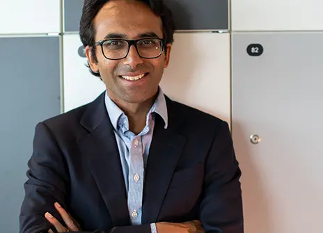 Ravi Gupta with his arms crossed, wearing a dark jacket and light shirt, smiling