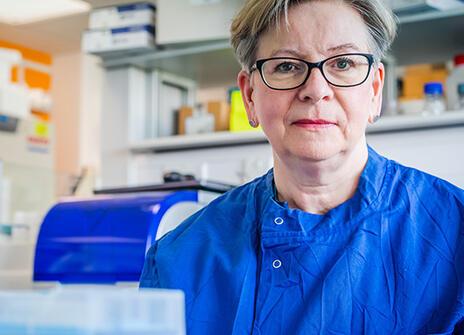 Sharon Peacock in a dark blue lab coat sitting behind a scientific apparatus