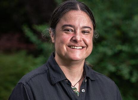 a woman with her dark hair tied back and wearing a black button up shirt and a jade spiral necklace