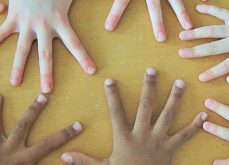 several pairs of hands with fingers outstretched covering a yellow surface