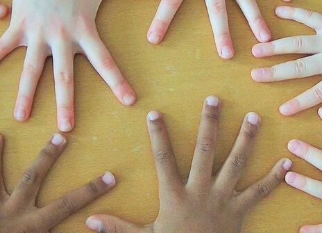 several pairs of hands with fingers outstretched covering a yellow surface