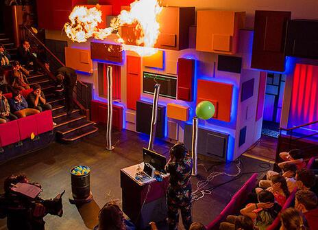 Christmas Lectures set with flames above it and an audience with hands over their ears